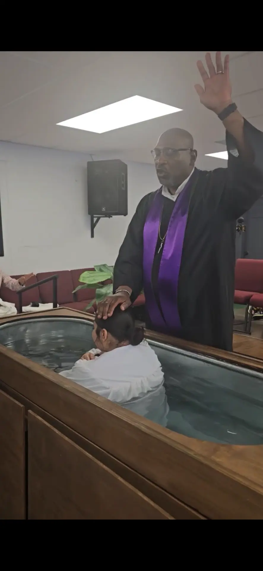 Pastor in a purple stole performing a baptism in a wooden basin